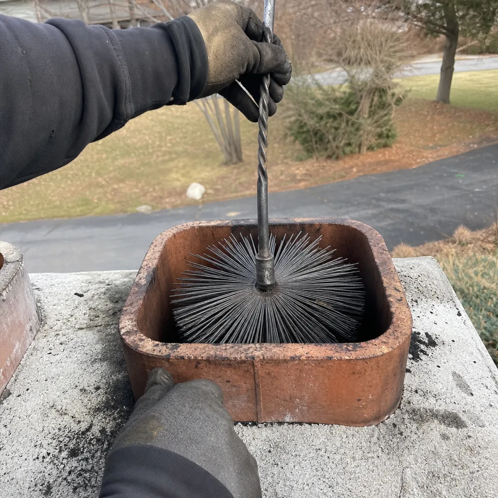 Professional technician performing residential chimney cleaning with a flue brush